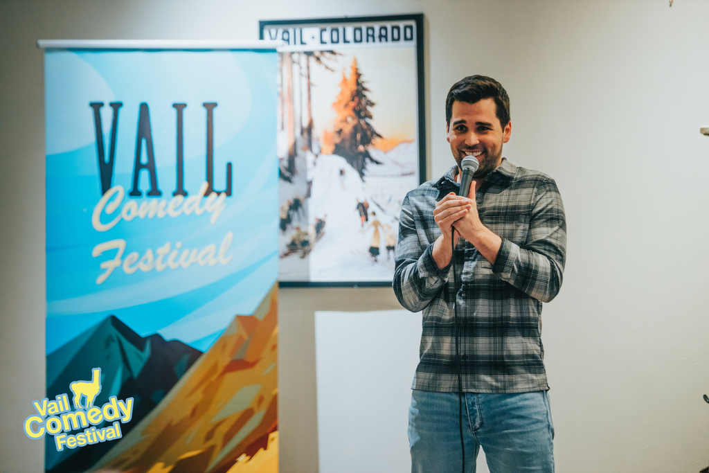 New York City comedian Kyle Mara performs at a pop up show at Cucina at The Lodge at Vail in front of a Vail Comedy Festival banner and a Vail, Colorado poster during the 2022 Vail Comedy Festival