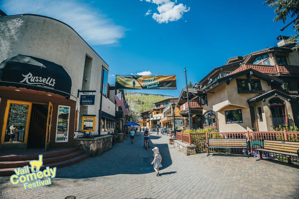 A future comedy fan enjoys Vail Village underneath a Vail Comedy Festival banner.  The 2022 Vail Comedy Festival had two sixteen foot wide banners.